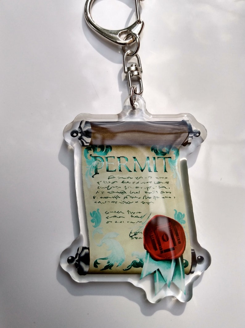 May include: A clear acrylic keychain featuring a scroll with the word "PERMIT" written on it. The scroll is decorated with a red wax seal and a green ribbon.