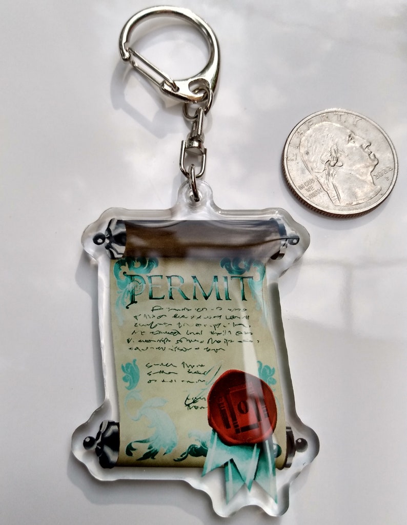 May include: A clear acrylic keychain featuring a scroll with the word "PERMIT" printed on it. The scroll is decorated with a red wax seal and a blue ribbon. The keychain is attached to a silver metal ring.