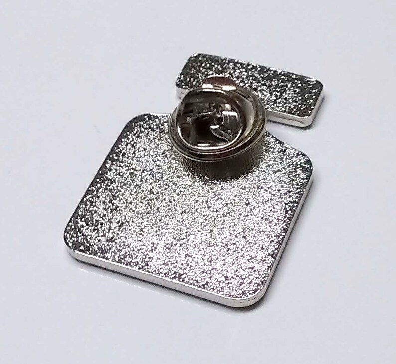 May include: Silver metal pin with a square shape and a pin back. The pin is blank.