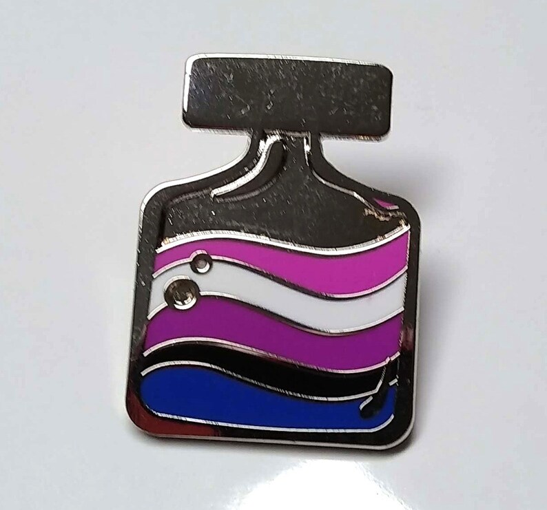 May include: A silver pin shaped like a bottle with a black top and a blue, black, white, pink and purple liquid inside. The liquid is in the shape of waves.