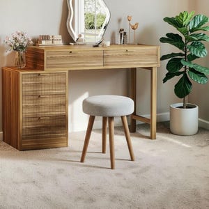 May include: A wooden vanity desk with two top drawers and a side cabinet featuring three drawers with textured fronts. A round, light grey upholstered stool with four wooden legs sits in front. An irregular mirror sits on the desk surface.