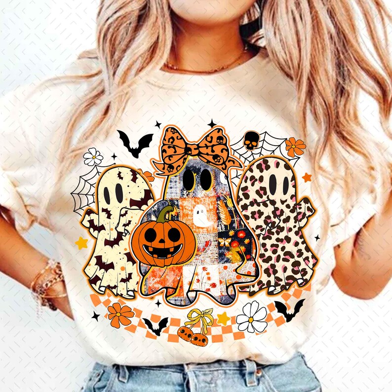 Peut inclure: T-shirt cr&egrave;me avec trois fant&ocirc;mes de dessins anim&eacute;s sur le th&egrave;me d'Halloween. Le fant&ocirc;me central tient une citrouille orange. Le t-shirt comprend des chauves-souris, des toiles d'araign&eacute;es et des motifs floraux.
