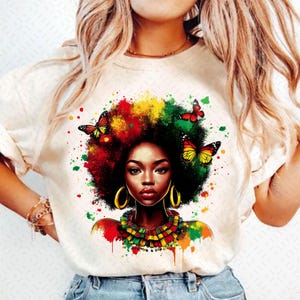 May include: A cream-coloured t-shirt with a colourful illustration of a woman with an afro, decorated with butterflies. The artwork uses red, yellow, and green hues, with gold hoop earrings and a matching necklace. The design is a striking display of art.