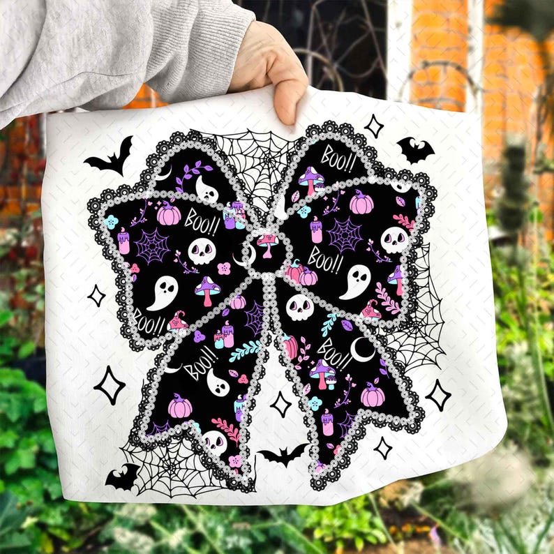 May include: A white Halloween-themed bow-shaped design with black, purple, and pink elements. The bow features skulls, ghosts, pumpkins, and the word "Boo!!" in a decorative font. The design is framed by a black lace-like border and spiderwebs.