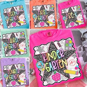 May include: A collection of colorful t-shirts featuring school-themed graphic prints. Each shirt displays a large black star with a composition notebook pattern, surrounded by illustrations of a globe, apple, pencil, paper, and smiley face stickers.