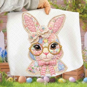 Pode incluir: Um design decorativo de coelhinho da Páscoa sobre um fundo branco. O coelhinho é adornado com óculos, uma gravata borboleta e um laço floral. As orelhas e o corpo do coelhinho são feitos de tecido patchwork em padrões rosa, azul e floral. O design é embelezado com pérolas.