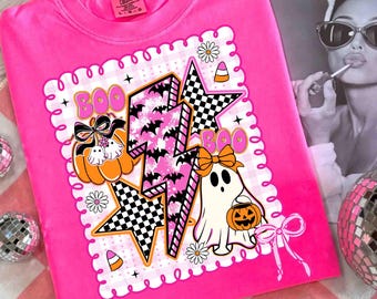 Puede incluir: Una camiseta rosa brillante con un diseño temático de Halloween. El diseño incluye una calabaza, un fantasma, estrellas y rayos, todo con el tema "Boo". El diseño incorpora patrones de cuadros blancos y negros, murciélagos y caramelos.
