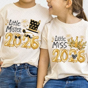 Può includere: Due magliette color crema con le scritte "Little Mister 2026" e "Little Miss 2026" in nero e oro. La maglietta "Mister" ha un cappello a cilindro e baffi. La maglietta "Miss" ha una corona.