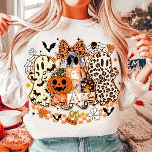 Peut inclure: Sweat-shirt blanc avec un motif sur le th&egrave;me d'Halloween. Le graphisme comprend trois fant&ocirc;mes, une citrouille sculpt&eacute;e, des chauves-souris, des toiles d'araign&eacute;es et des motifs floraux. Les fant&ocirc;mes ont divers motifs, dont l'imprim&eacute; l&eacute;opard et le patchwork.