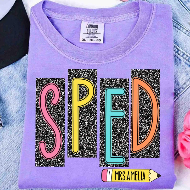 May include: A lavender Comfort Colors t-shirt with the word "SPED" in colorful block letters. The letters are set against a black and white speckled background. A pencil graphic with the text "MRS. AMELIA" is below the letters.