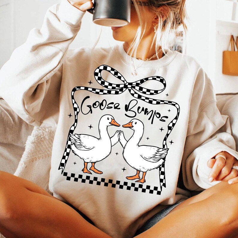May include: A white sweatshirt featuring a black and white chequered bow and the text "Goose Bumps". Two white geese are facing each other with their wings outstretched.