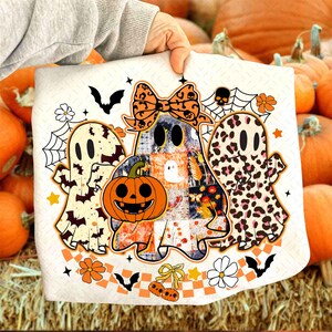 Peut inclure: Un coussin blanc sur le th&egrave;me d'Halloween avec trois fant&ocirc;mes de dessins anim&eacute;s, une citrouille sculpt&eacute;e, des chauves-souris, des toiles d'araign&eacute;es et des motifs floraux. Les fant&ocirc;mes ont des motifs uniques, dont un patchwork et un imprim&eacute; l&eacute;opard.