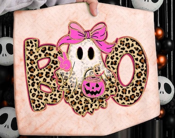 May include: A pink and tan Halloween-themed sign with the word "BOO" in leopard print. The "O" is a ghost holding a jack-o'-lantern and wearing a pink bow. The ghost is giving a peace sign.