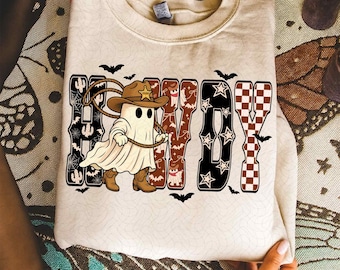 Könnte beinhalten: Cremefarbenes Sweatshirt mit einem Cowboy-Geist, der einen Lasso hält, Hut und Stiefel trägt. Das Wort "HOWDY" ist in einer dekorativen Schriftart mit Halloween-Akzenten und Fledermäusen geschrieben.
