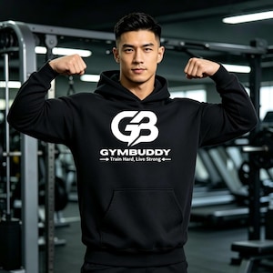 Op de afbeelding: Een zwarte hoodie met een wit grafisch logo op de borst met de tekst GYMBUDDY, vergezeld van de tekst Train Hard, Live Strong en pijlen die naar buiten wijzen. De trui is voorzien van een kangoeroezak en lange mouwen met boorden.