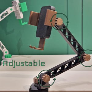 Peut inclure: Un support de téléphone articulé noir avec des boutons de réglage marron et un berceau de téléphone marron. Le mot Adjustable est imprimé en vert. Le support présente un bras en treillis avec plusieurs points de pivot. Un second support blanc et vert est visible en arrière-plan.