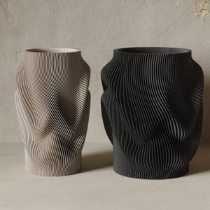 May include: Two cylindrical vases, one light beige and one matte black, featuring a distinct vertical ribbed texture with a fluid, undulating wave pattern that creates a sense of movement across the exterior surface of each vessel.