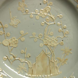 May include: A light blue ceramic plate with a white floral design. The design features delicate branches with small white flowers and leaves.