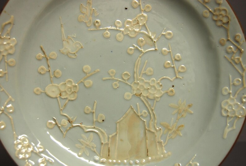 May include: A light blue ceramic plate with a white floral design. The design features delicate branches with small white flowers and leaves.