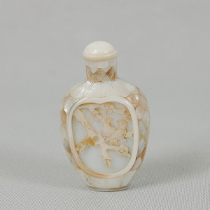 Puede incluir: Una botella decorativa nacarada con un diseño tallado de un pájaro en una rama. La botella está cubierta de pequeñas piezas de concha iridiscentes y tiene una tapa a juego. El diseño tallado está enmarcado.