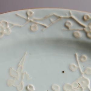 May include: A light blue ceramic plate with white floral designs. The plate has a raised rim and a smooth surface.