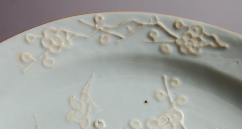May include: A light blue ceramic plate with white floral designs. The plate has a raised rim and a smooth surface.