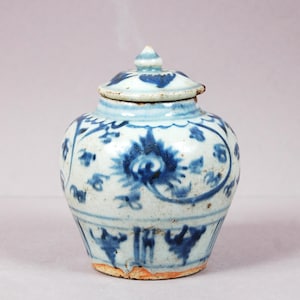Peut inclure: Un petit pot en céramique arrondi avec un couvercle assorti, orné d'un motif floral et végétal bleu peint à la main sur un fond émaillé blanc cassé. Le récipient présente un corps large, un col court et un bouton pointu sur le couvercle.