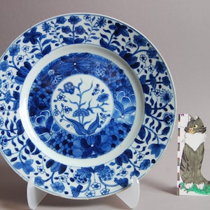 Op de afbeelding: Een blauw en wit porseleinen bord met een bloemenmotief. Het bord heeft een centraal bloemenmotief omgeven door een rand met kleinere bloemenmotieven.