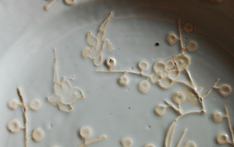 May include: A white ceramic plate with a delicate floral design. The design features white flowers and leaves on a light blue background.