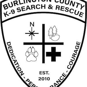 Op de afbeelding: Een zwart-wit schildvormig embleem voor Burlington County K-9 Search & Rescue. Het ontwerp bevat een kompasroos, een pootafdruk, een kruis en bomen. De woorden "DEDICATION - PERSEVERANCE - COURAGE" en "EST. 2010" zijn ook aanwezig.