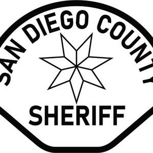May include: A white shield-shaped patch with a thick black border. The text SAN DIEGO COUNTY is arched across the top, and the word SHERIFF is printed at the bottom in black. A black six-pointed star emblem is centered between the text elements.