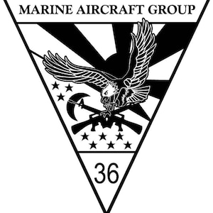 May include: A black and white Marine Aircraft Group emblem. The emblem features an eagle with outstretched wings above crossed rifles and a crescent moon. The number 36 is at the bottom. The text "MARINE AIRCRAFT GROUP" is at the top.