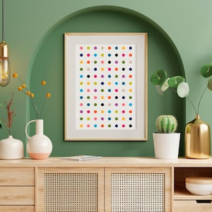 May include: A framed art print featuring a grid of colorful polka dots in various hues, including red, blue, green, and yellow. The artwork is displayed on a wooden cabinet with decorative vases and a small cactus in a white pot. The background is a green wall.