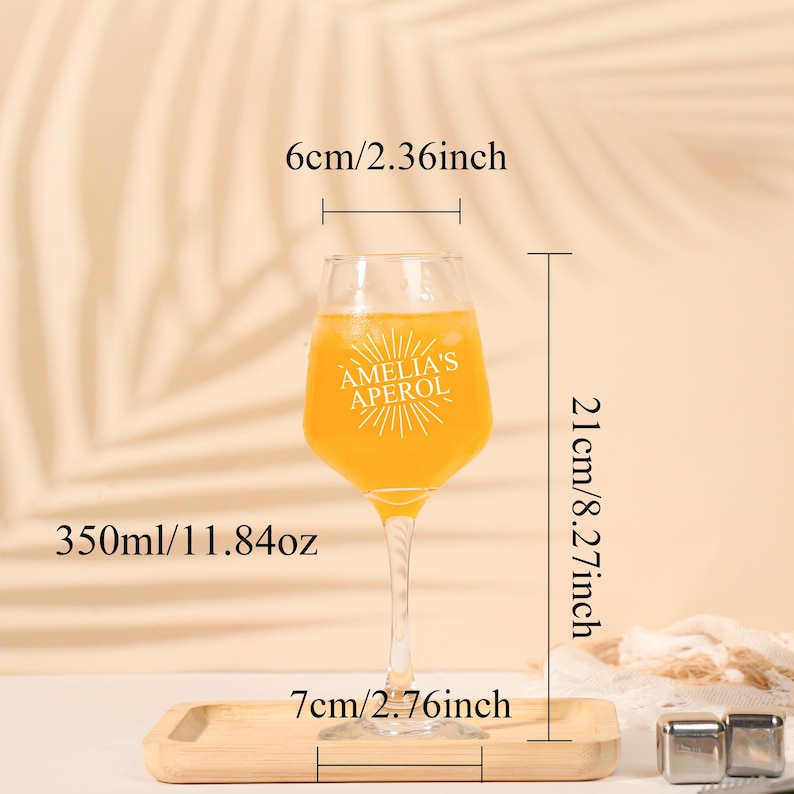 May include: A clear wine glass filled with an orange liquid, labeled "AMELIA'S APEROL". The glass is 8.27 inches tall, 2.36 inches wide, and holds 11.84 oz. It sits on a wooden tray that is 2.76 inches wide.