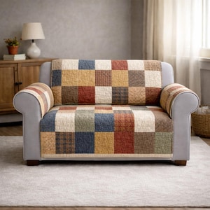Può includere: Un divano grigio a due posti con una copertura trapuntata patchwork. La copertura presenta quadrati di vari colori, tra cui rosso, blu, giallo e marrone. I braccioli del divano sono grigi e le gambe sono in legno.