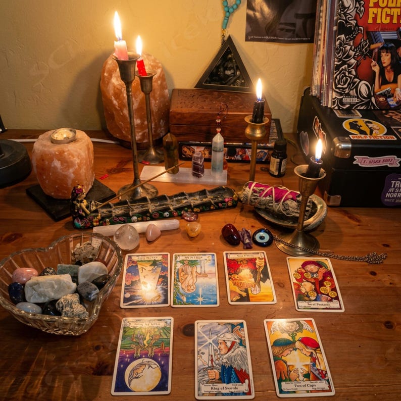 May include: A wooden table displays a spiritual setup with lit candles in brass holders, tarot cards, crystals, and a heart-shaped bowl of stones. A wooden box, incense, and a vintage record player are also present.