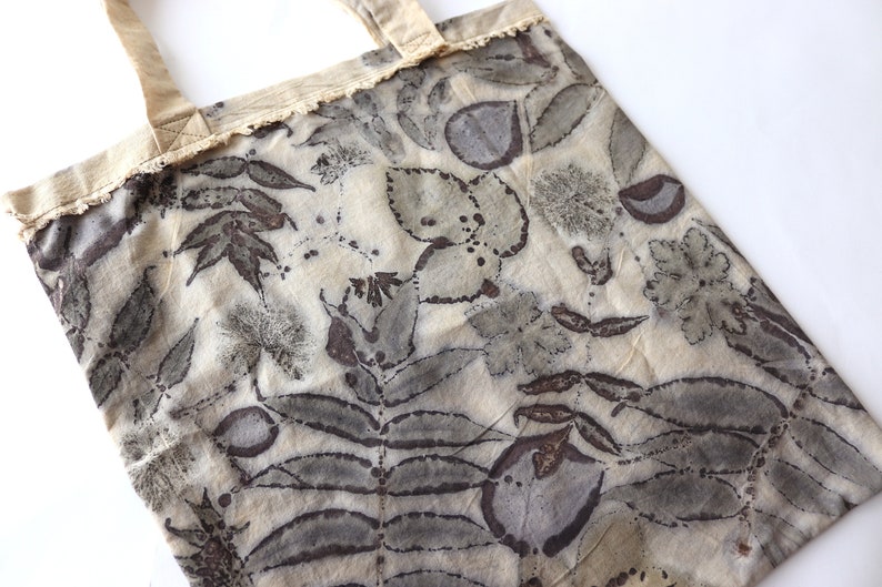Puede incluir: Una bolsa de tela beige con un ribete de encaje y un estampado bot&aacute;nico en tonos marrones y grises.