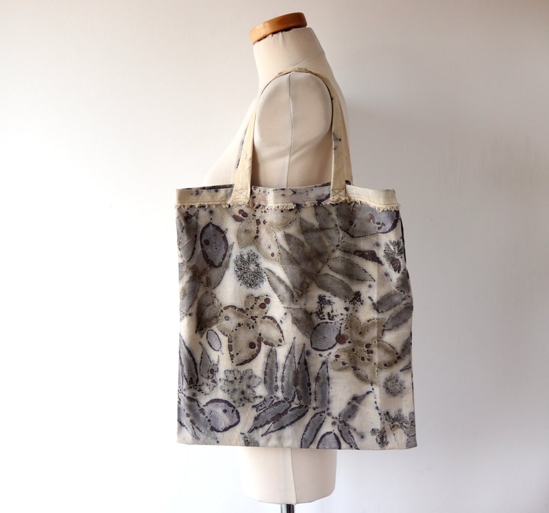 Puede incluir: Una bolsa de tela beige con un patr&oacute;n de hojas y flores te&ntilde;idas naturalmente en tonos marrones, grises y blancos.