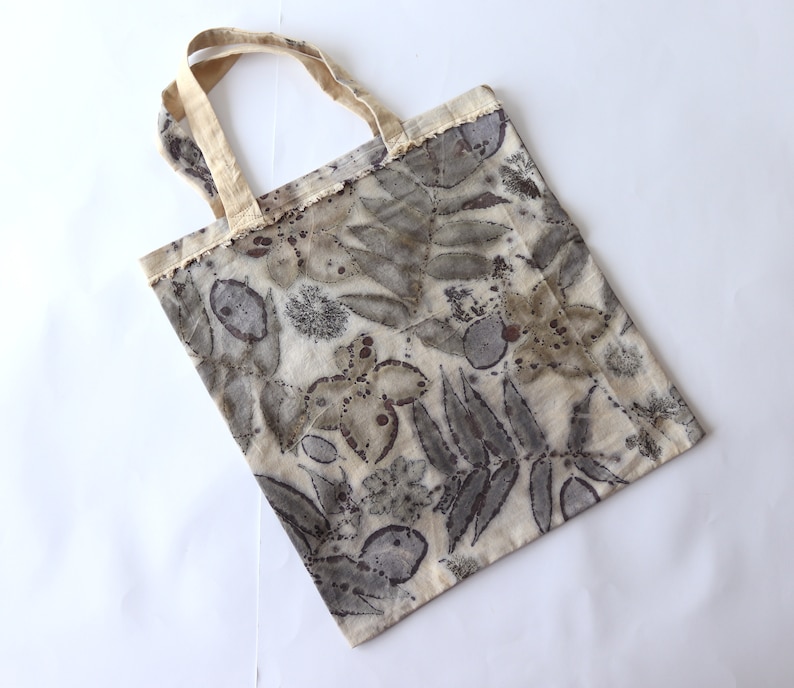 Puede incluir: Una bolsa de tela beige con un estampado de hojas y flores en tela natural en tonos marrones y grises. La bolsa tiene un asa de tela natural.