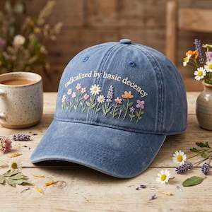 May include: A white ceramic mug with a black handle and the text "But First, Coffee" in a bold, black font. The mug is set against a blurred background, highlighting its clean design.