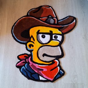 Könnte beinhalten: Ein farbenfroher Teppich mit einer Cartoonfigur, die einen Cowboyhut, eine Brille und ein rotes Halstuch trägt. Der Teppich hat ein gelbes Gesicht, einen braunen Hut und blaue und rote Kleidung. Der Teppich liegt auf einem hellen Holzboden.