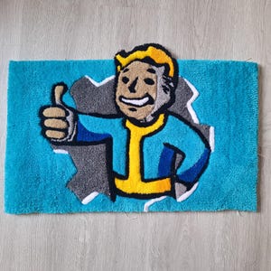 May include: A blue bath mat with a cartoon character of a man with yellow hair and a blue jumpsuit. The man is giving a thumbs up and is partially sticking out of a hole in the mat.