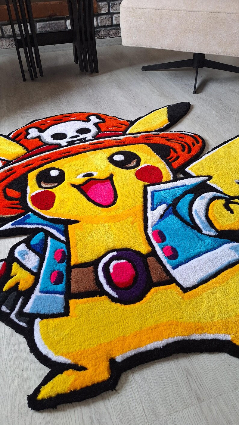 K&ouml;nnte beinhalten: Ein getufteter Teppich in Form einer gelben Figur, die einen roten Strohhut mit einem wei&szlig;en Totenkopf-Emblem, eine blaue Jacke und einen braunen G&uuml;rtel mit runder Schnalle tr&auml;gt. Die Figur hat rote Wangen, ein breites L&auml;cheln und schwarze Ohrspitzen.