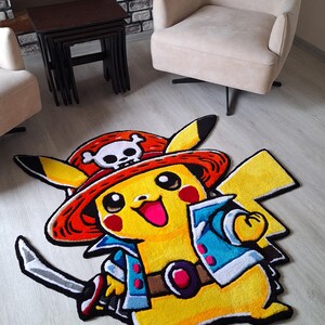 K&ouml;nnte beinhalten: Ein getufteter Teppich in Form der Figur Pikachu, die einen roten Piratenhut mit wei&szlig;em Totenkopf-Emblem, eine blaue Jacke und einen braunen G&uuml;rtel tr&auml;gt und ein silbernes Schwert mit schwarzem Griff und roten Akzenten auf dem Boden h&auml;lt.