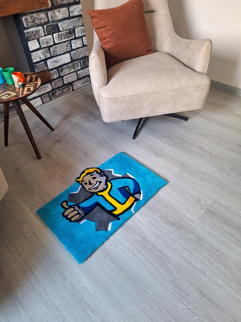 May include: A blue rug with a cartoon character from the Fallout video game series. The character is wearing a blue jumpsuit and a yellow utility belt. The character is giving a thumbs up. The rug is on a light wood floor.