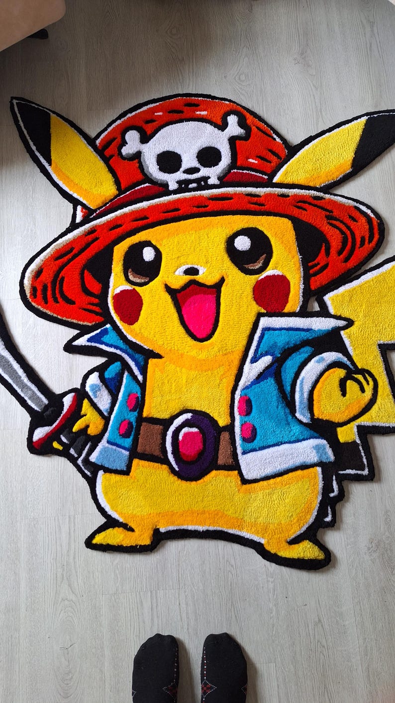 K&ouml;nnte beinhalten: Ein gelber getufteter Teppich in Form einer Figur, die einen roten Strohhut mit einem wei&szlig;en Totenkopf-Emblem tr&auml;gt. Die Figur hat rote Wangen, eine blaue Jacke mit wei&szlig;em Saum, einen braunen G&uuml;rtel mit einem roten Edelstein und h&auml;lt ein Schwert.