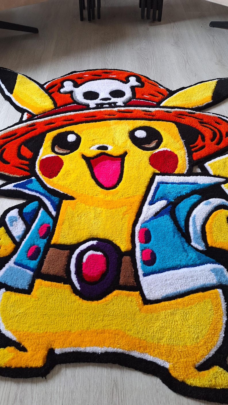 K&ouml;nnte beinhalten: Ein getufteter Teppich in Form einer gelben Figur mit schwarz gespitzten Ohren, die einen roten Strohhut mit wei&szlig;em Totenkopf-Emblem, eine offene blaue Jacke und einen braunen G&uuml;rtel mit einer violetten und rosafarbenen Schnalle tr&auml;gt.