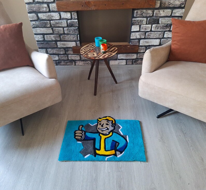 May include: A blue rug with a cartoon character from the video game Fallout. The character is wearing a blue jumpsuit and has a yellow collar. The character is giving a thumbs up. The rug is on a light brown floor in front of a white couch and a wooden coffee table.