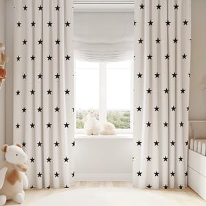 Puede incluir: Cortinas blancas con un patrón de estrellas negras cuelgan en una guardería con una cuna blanca y animales de peluche.