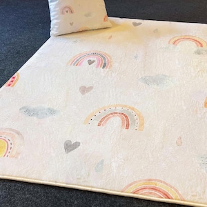 May include: A white plush rug with a repeating pattern of colorful rainbows, clouds, and hearts. The rug has a cream-colored border.